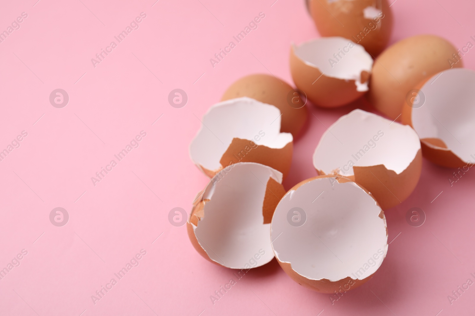 Photo of Broken eggshells on pink background, closeup. Space for text