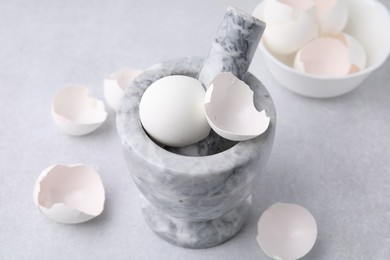 Photo of Broken eggshells, mortar and pestle on grey table, closeup