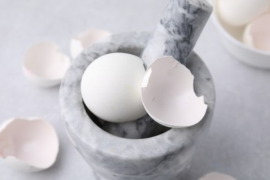 Photo of Broken eggshells, mortar and pestle on grey table, closeup