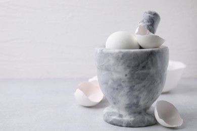 Photo of Broken eggshells, mortar and pestle on grey table, closeup. Space for text