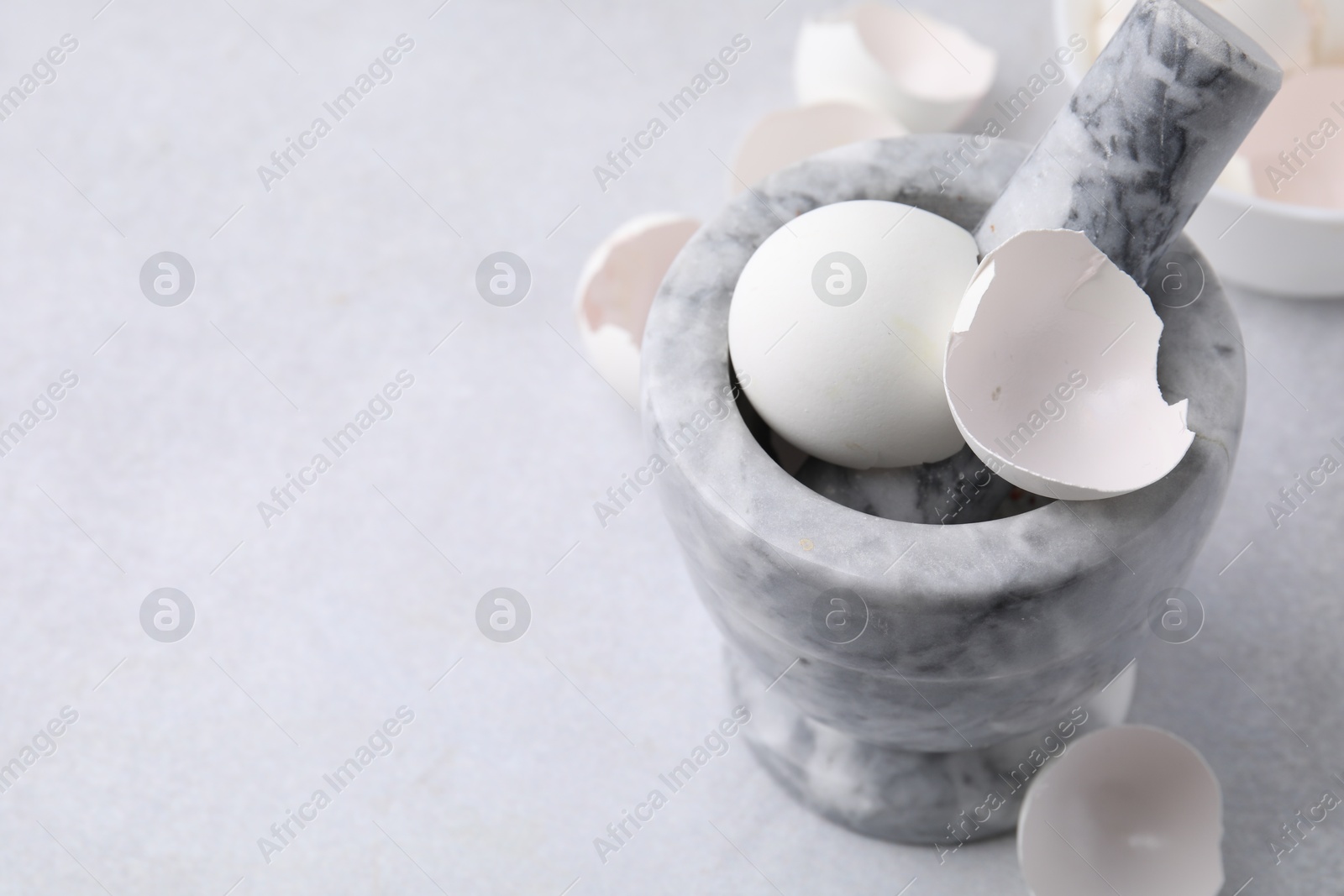 Photo of Broken eggshells, mortar and pestle on grey table, closeup. Space for text