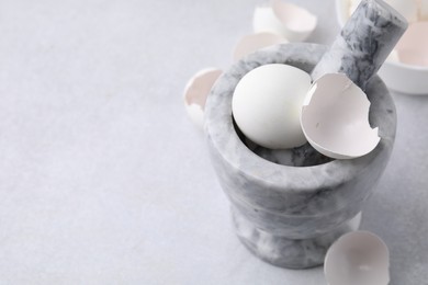 Photo of Broken eggshells, mortar and pestle on grey table, closeup. Space for text