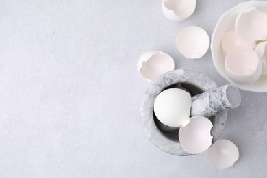 Photo of Broken eggshells, mortar and pestle on grey table, flat lay. Space for text