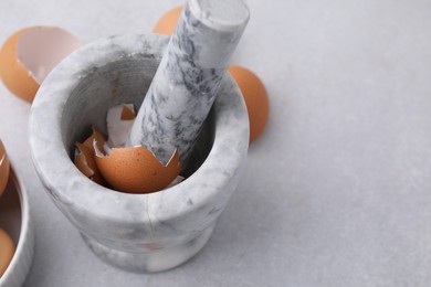 Photo of Broken eggshells, mortar and pestle on grey table, closeup. Space for text