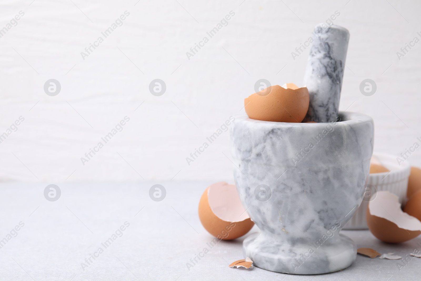 Photo of Broken eggshells, mortar and pestle on grey table, closeup. Space for text