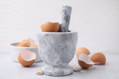 Photo of Broken eggshells, mortar and pestle on grey table, closeup