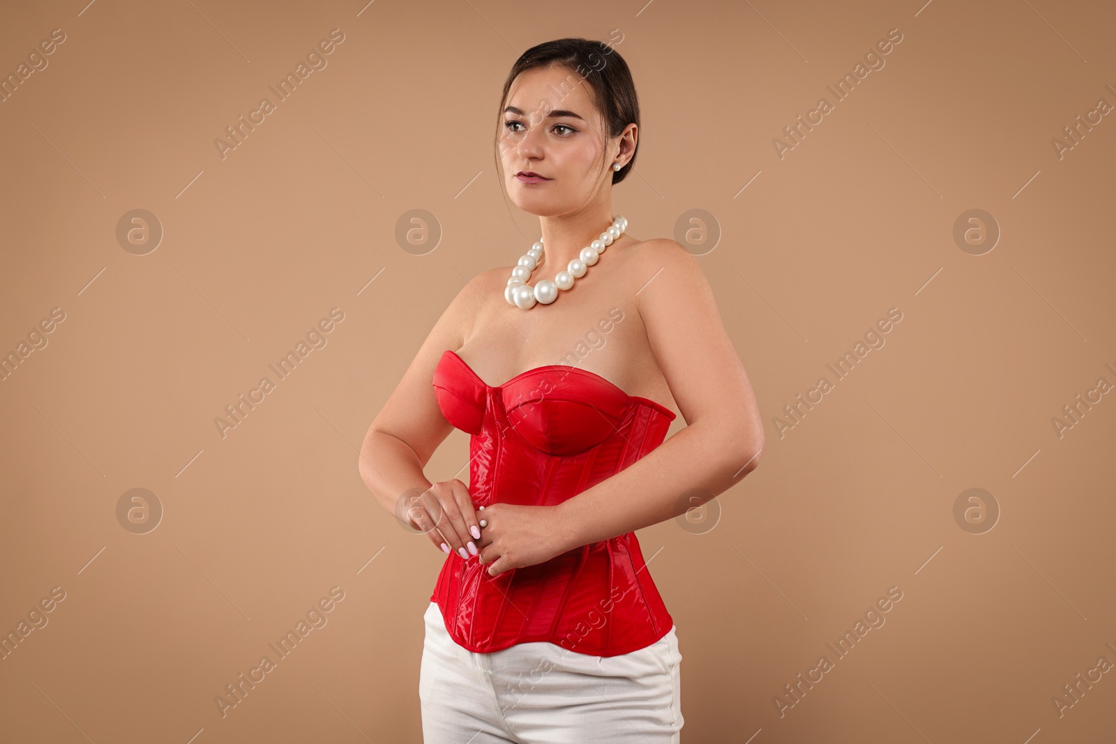 Photo of Beautiful woman in red corset posing on beige background