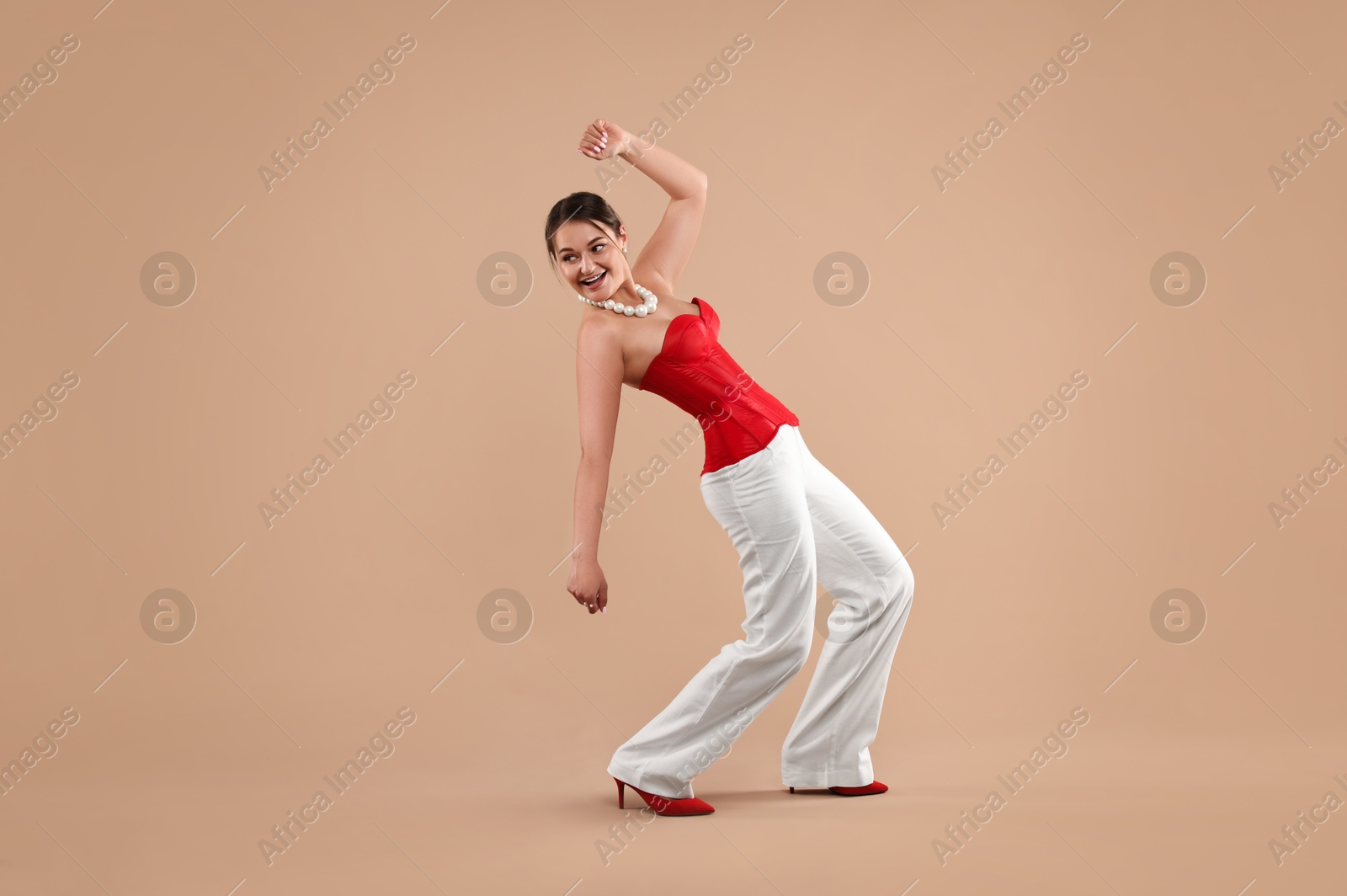 Photo of Smiling woman in red corset posing on beige background. Space for text