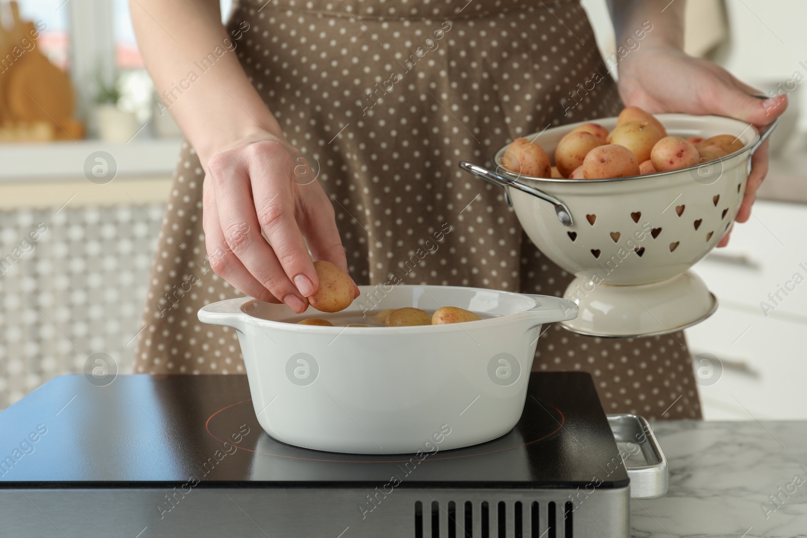 Photo of Woman putting potato into metal pot on stove, closeup