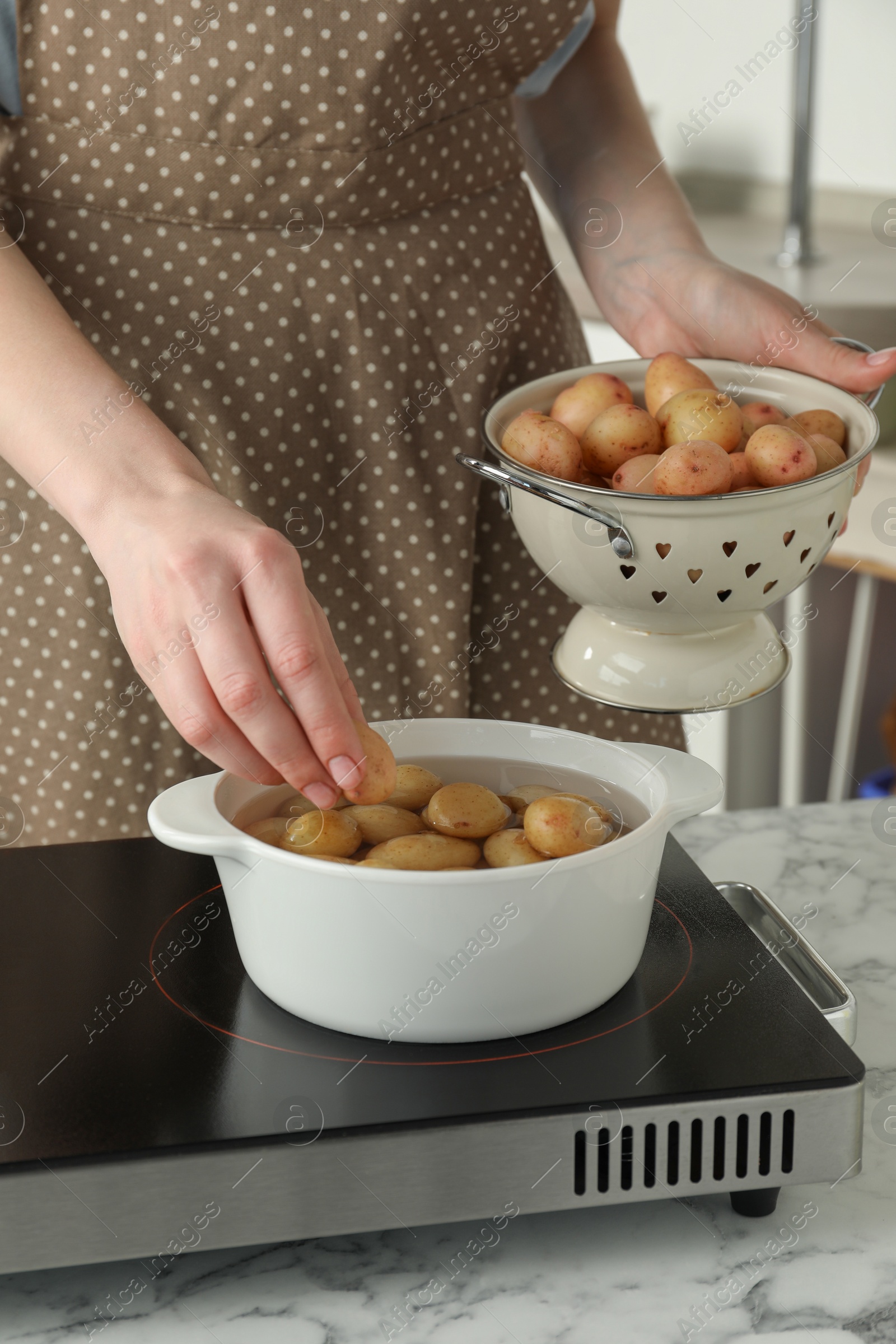 Photo of Woman putting potato into metal pot on stove, closeup