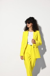 Photo of Beautiful young woman in stylish yellow suit and sunglasses on light background