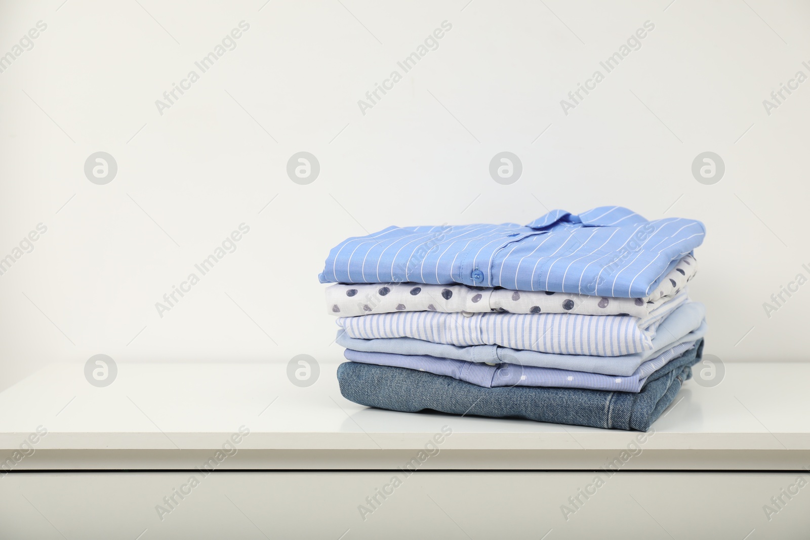 Photo of Stack of clothes on white shelf indoors, space for text