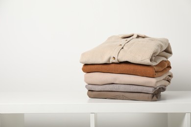 Photo of Stack of clothes on white shelf indoors, space for text