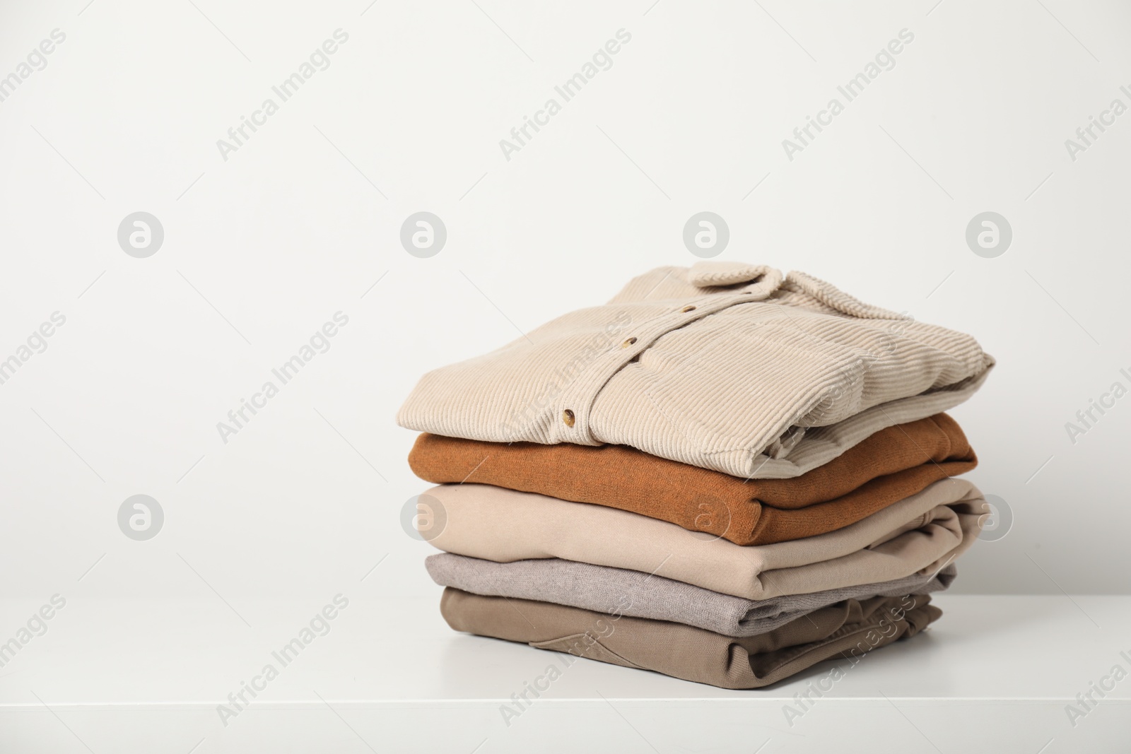 Photo of Stack of clothes on white shelf indoors, space for text