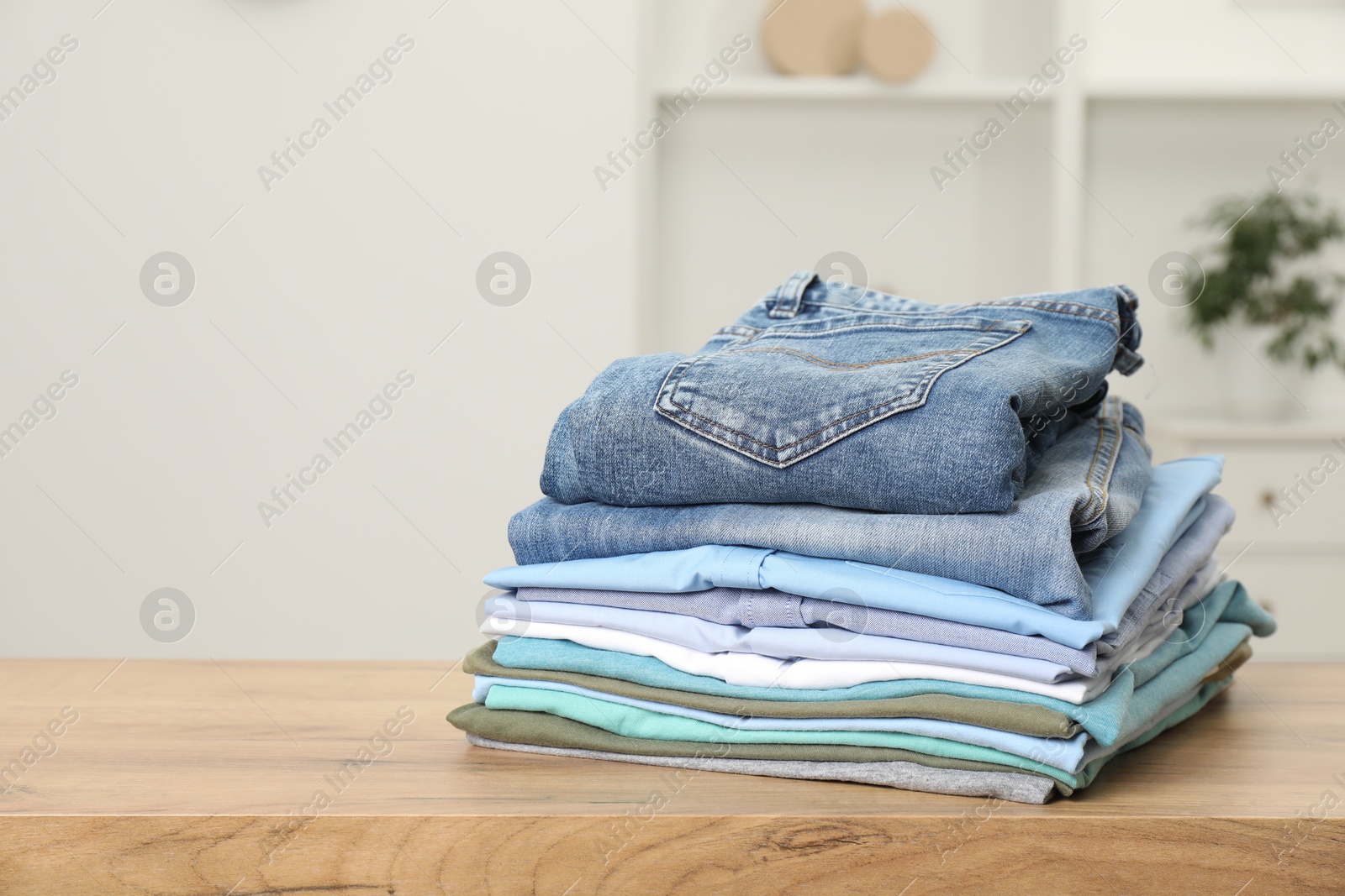 Photo of Stack of clothes on wooden table indoors, space for text