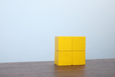 Photo of Many blank yellow cubes on wooden table against light blue background, space for text