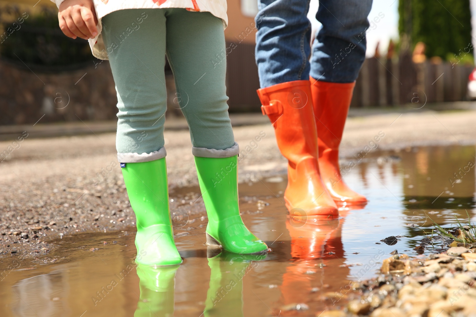 Photo of Mother and daughter wearing rubber boots standing in puddle outdoors, closeup