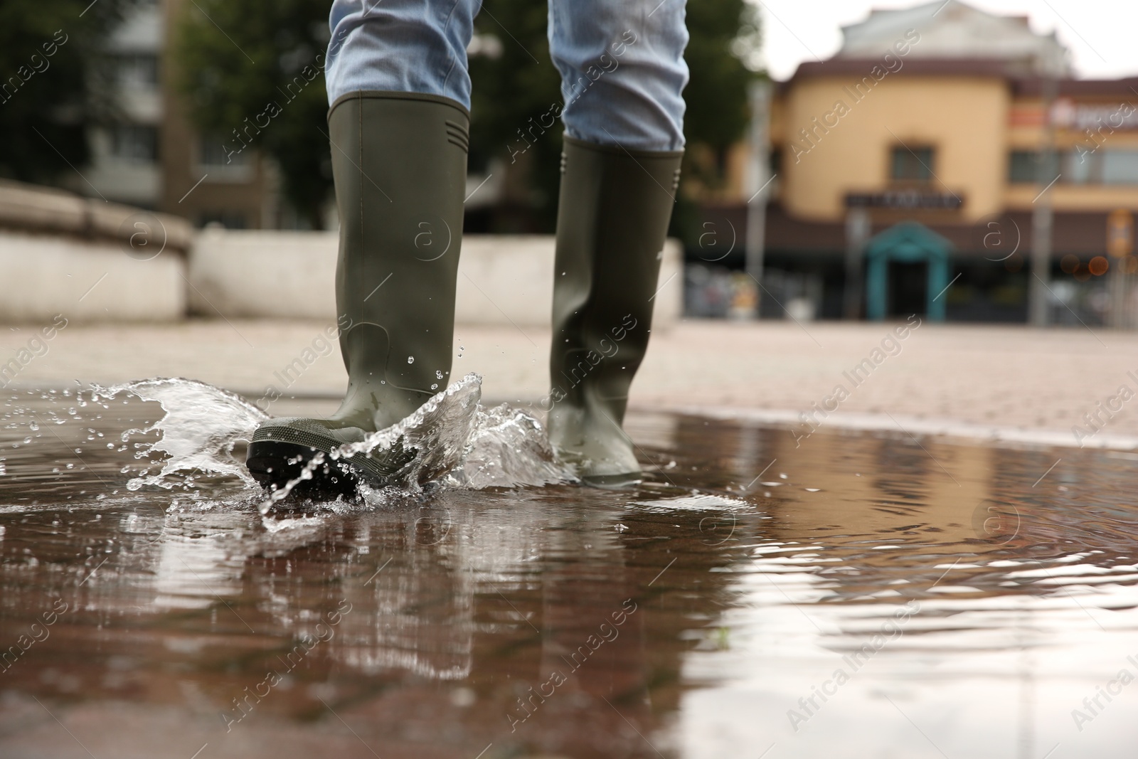 Photo of Woman wearing rubber boots walking in puddle outdoors, closeup