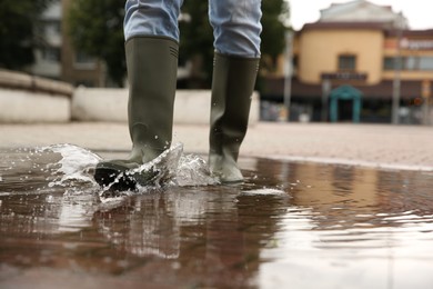 Woman wearing rubber boots walking in puddle outdoors, closeup