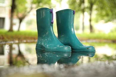 Photo of Pair of colorful rubber boots in puddle outdoors