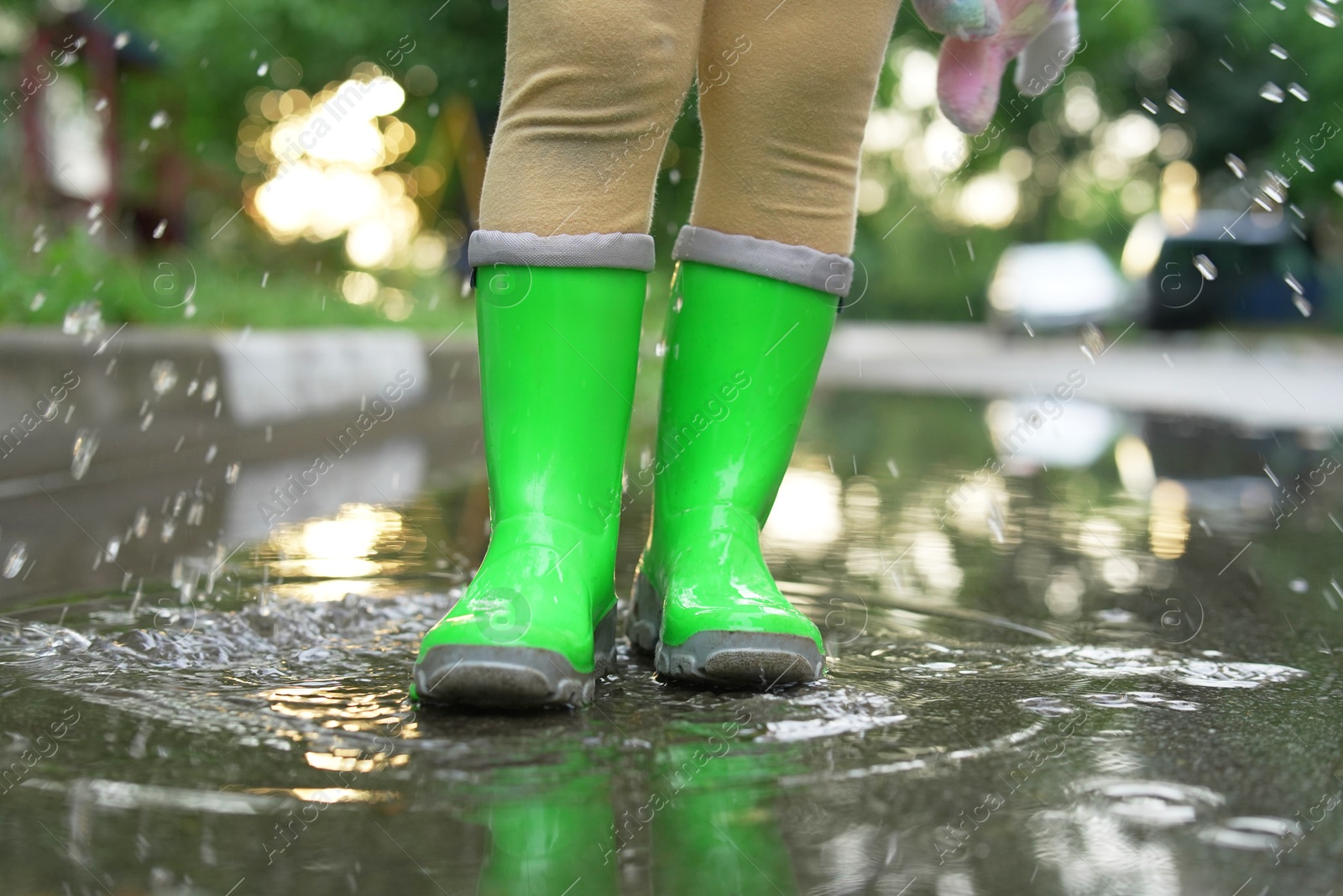 Photo of Little girl wearing green rubber boots standing in puddle outdoors, closeup