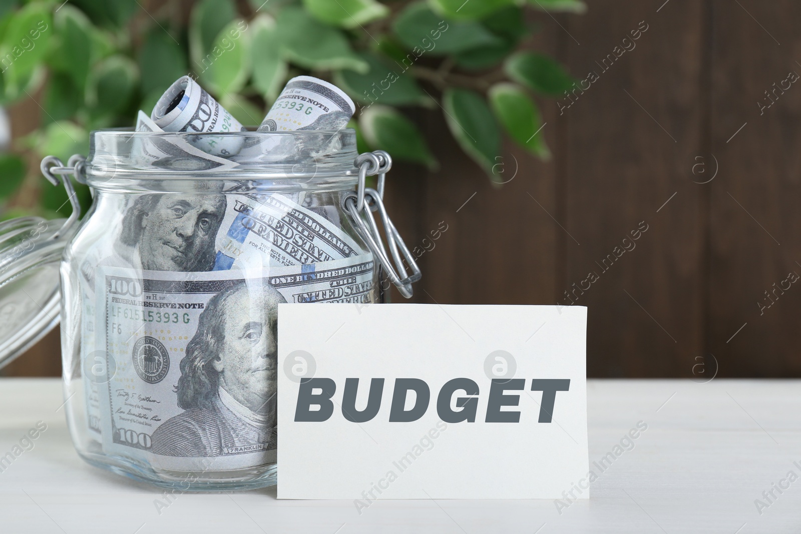 Image of Card with word Budget and glass jar full of money on white table