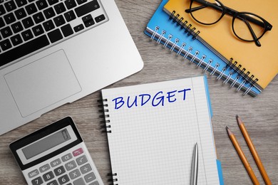 Image of Notebook with word Budget, calculator, glasses and laptop on wooden table, flat lay