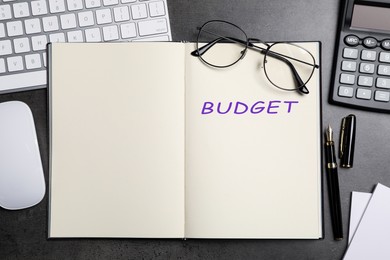 Image of Notebook with word Budget, calculator, glasses, keyboard and mouse on dark table, flat lay