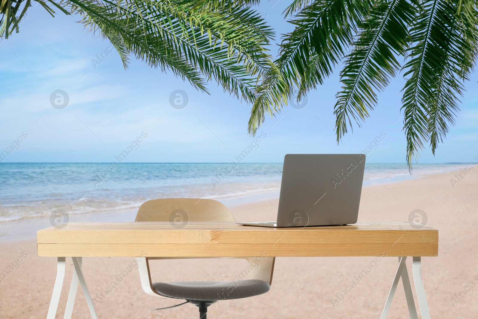 Image of Workplace at beach, distant office. Table with laptop and chair on sandy seashore