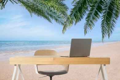 Workplace at beach, distant office. Table with laptop and chair on sandy seashore