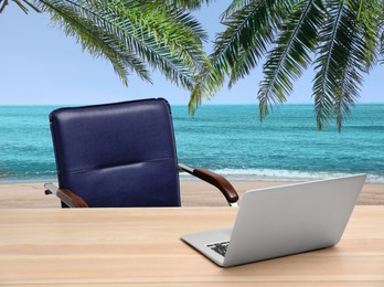 Image of Workplace at beach, distant office. Table with laptop and chair on sandy seashore