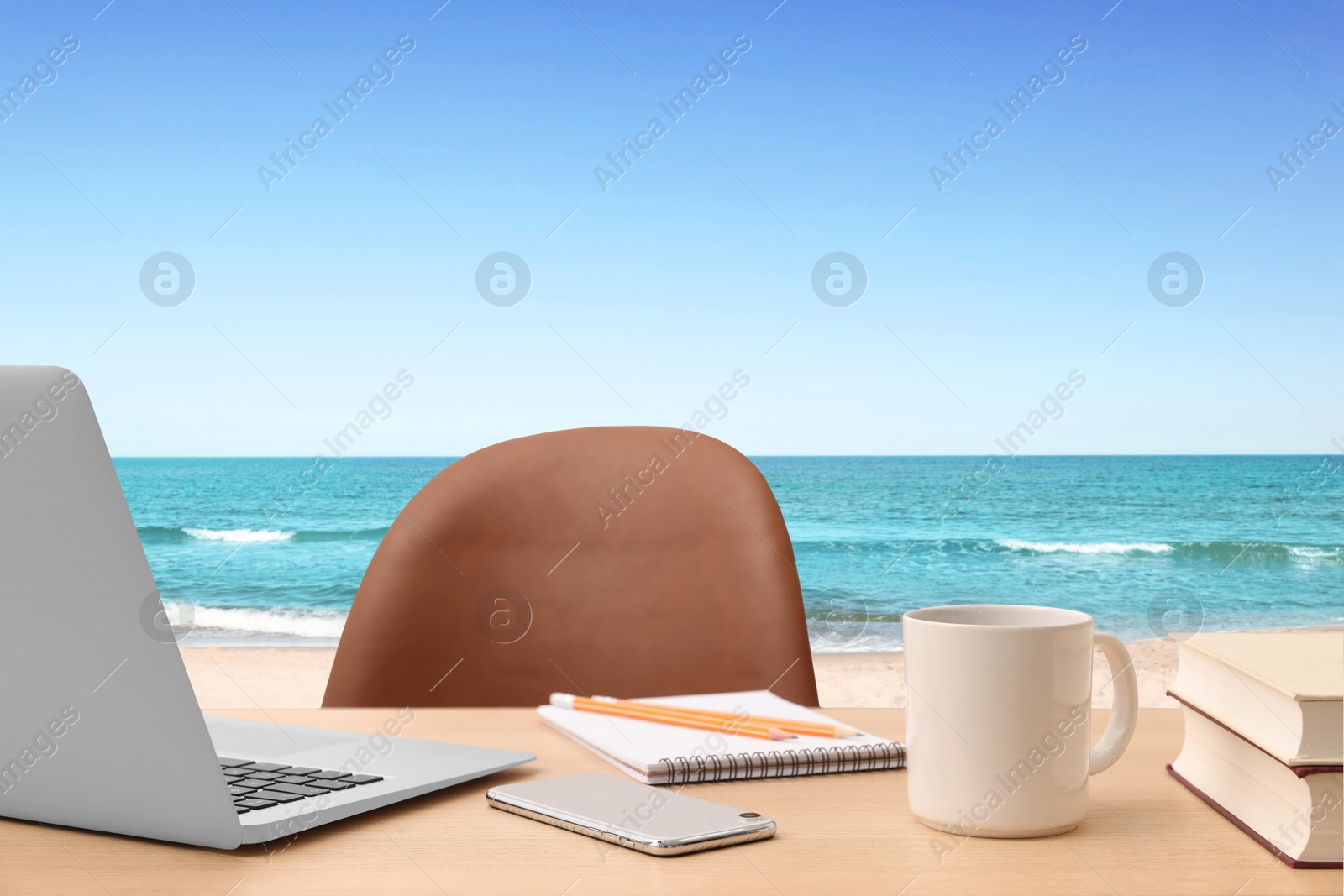 Image of Workplace at beach, distant office. Table with laptop and chair on sandy seashore