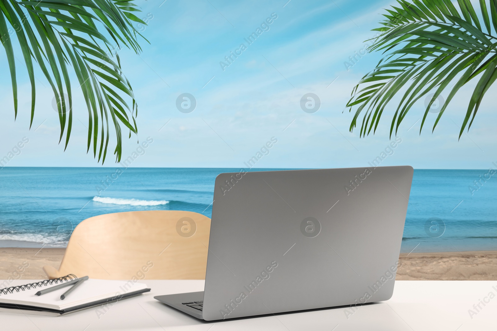 Image of Workplace at beach, distant office. Table with laptop and chair on sandy seashore