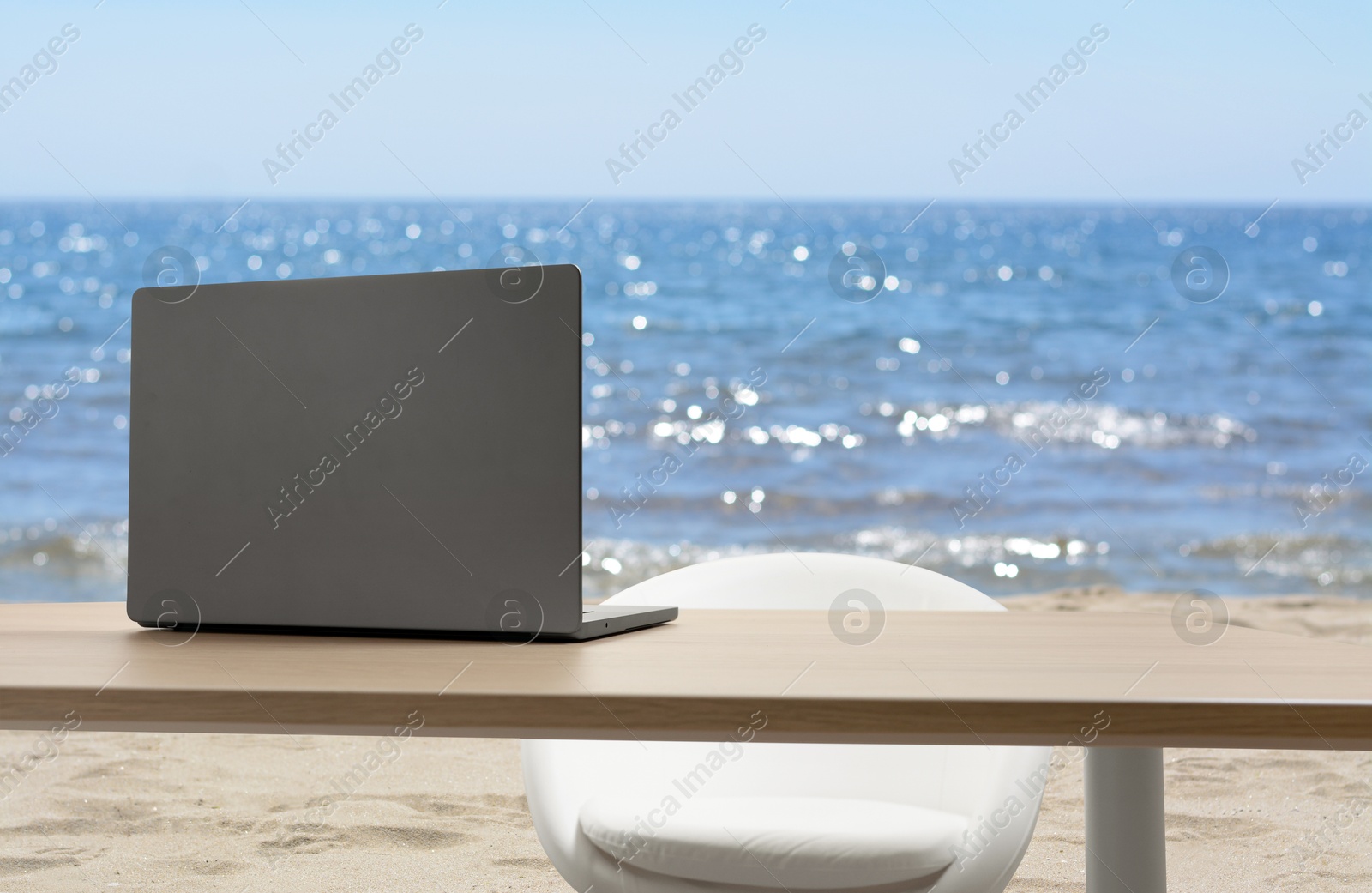 Image of Workplace at beach, distant office. Table with laptop and chair on sandy seashore