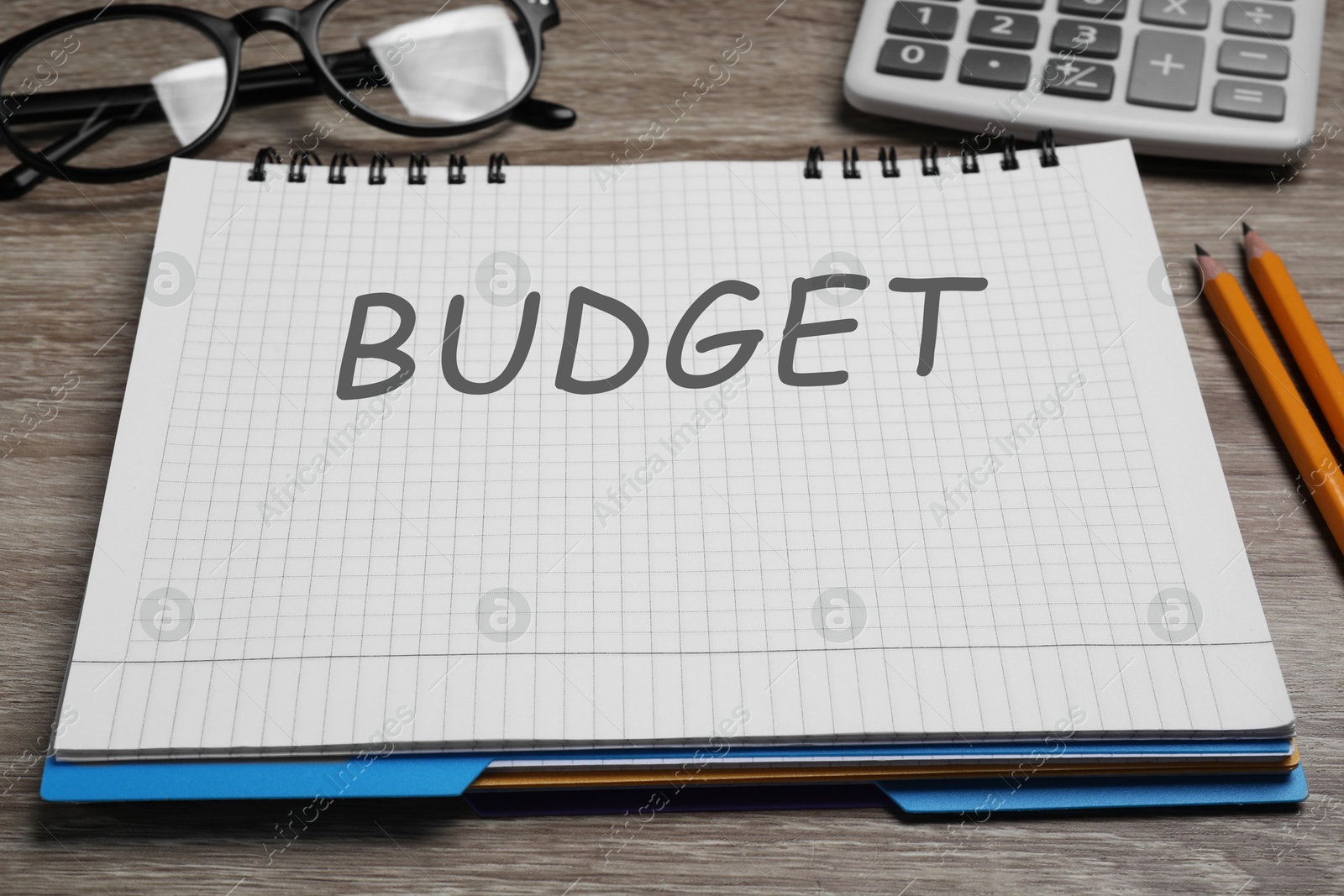 Image of Notebook with word Budget, calculator and glasses on wooden table, closeup