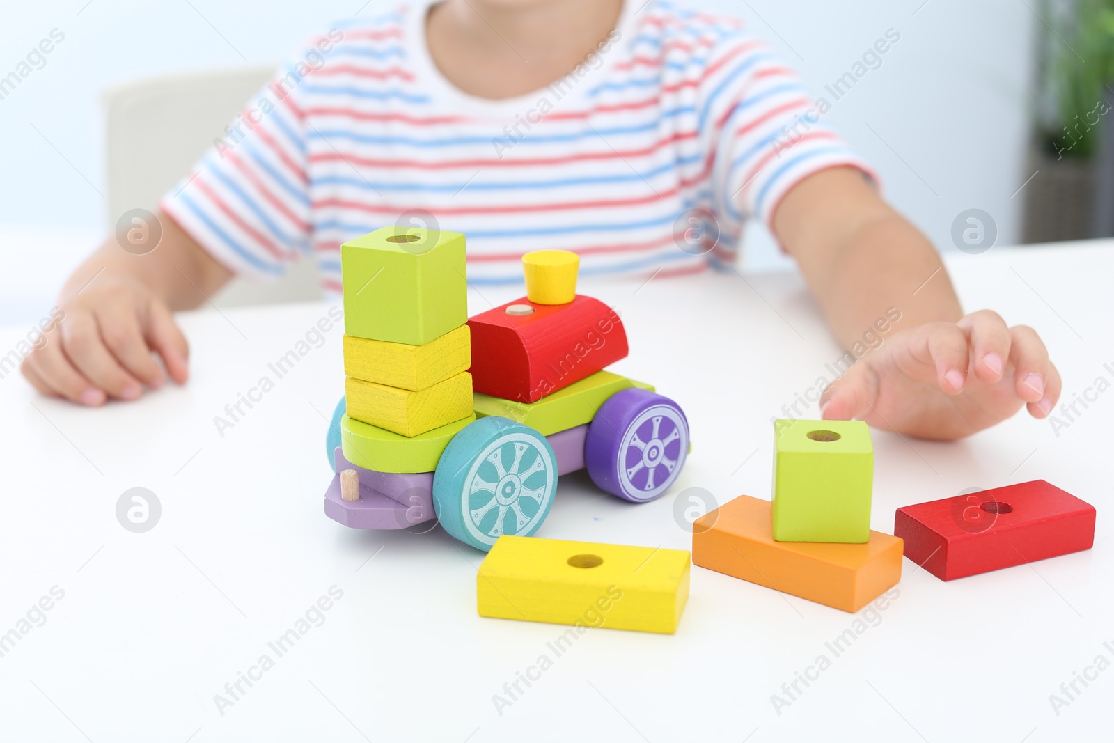 Photo of Little boy playing with toy at white table, closeup