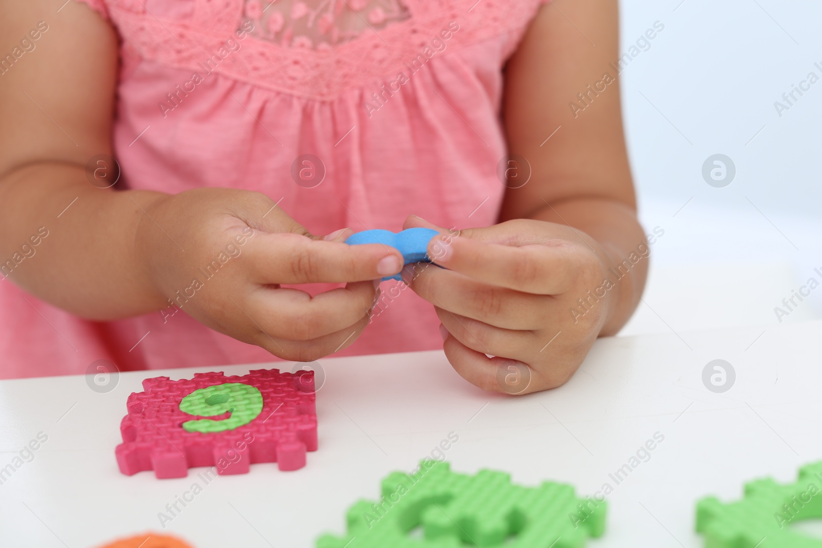 Photo of Little girl playing with colorful puzzles at white table, closeup. Educational toy