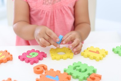 Little girl playing with colorful puzzles at white table, closeup. Educational toy