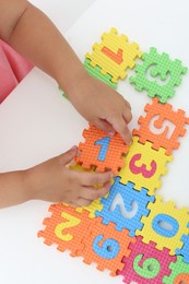 Photo of Little girl playing with colorful puzzles at white table, top view. Educational toy