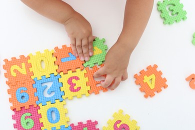 Little girl playing with colorful puzzles at white table, top view. Educational toy