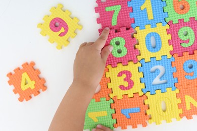 Photo of Little girl playing with colorful puzzles at white table, top view. Educational toy