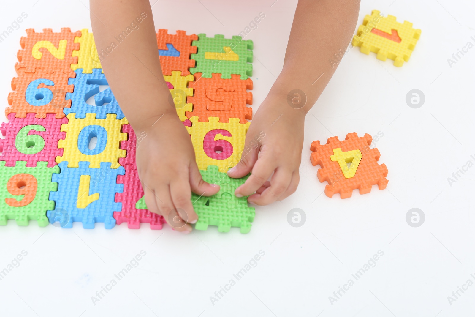 Photo of Little girl playing with colorful puzzles at white table, closeup. Educational toy