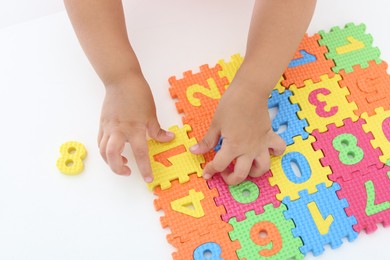 Little girl playing with colorful puzzles at white table, closeup. Educational toy