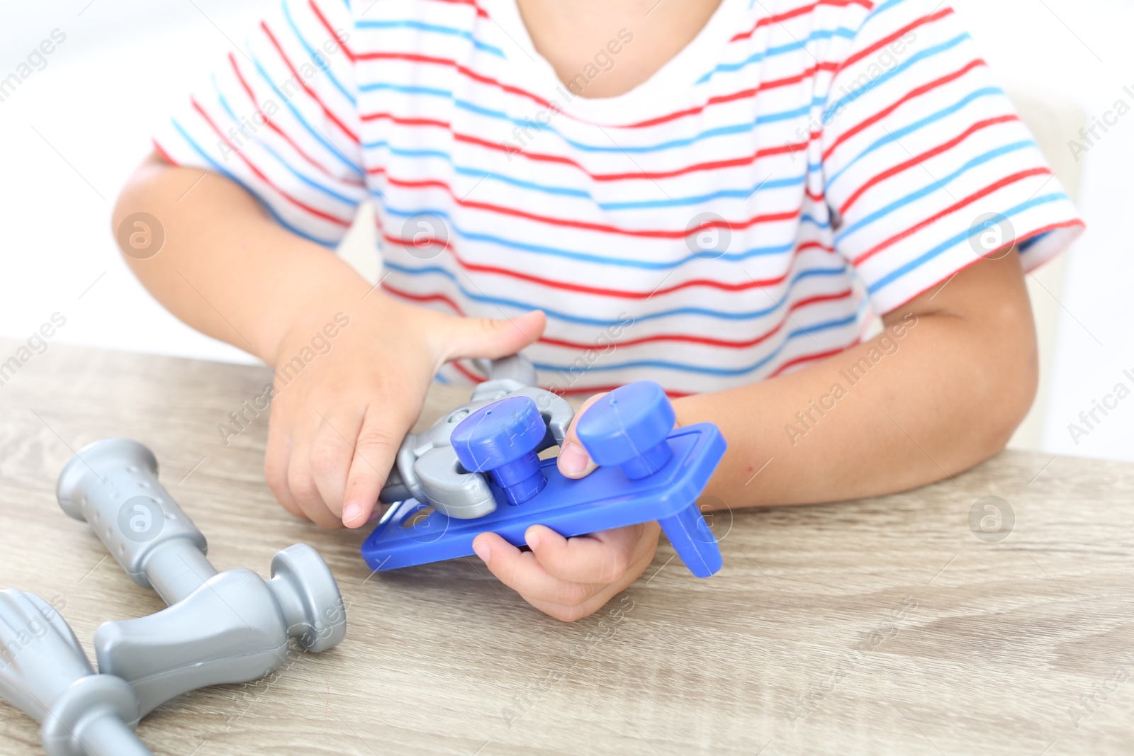 Photo of Little boy playing with toy construction tools at wooden table, closeup