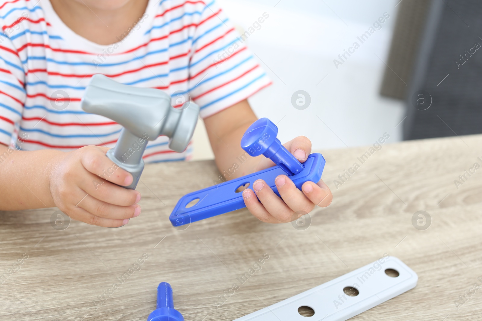 Photo of Little boy playing with toy construction tools at wooden table, closeup