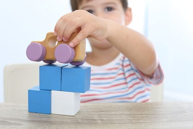 Photo of Little boy playing with toys at wooden table, focus on hand