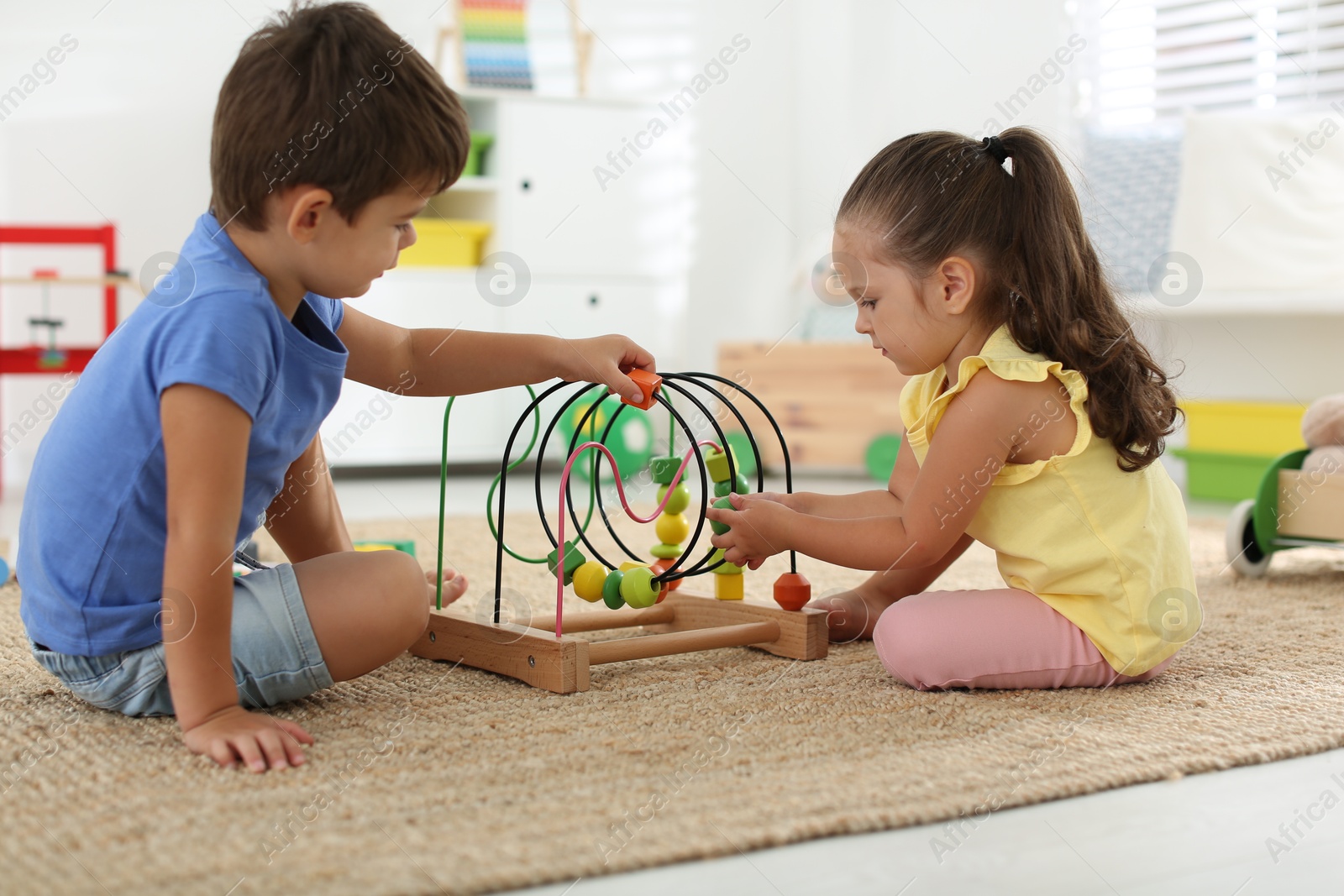 Photo of Cute little children playing with bead maze on floor at home. Educational toy