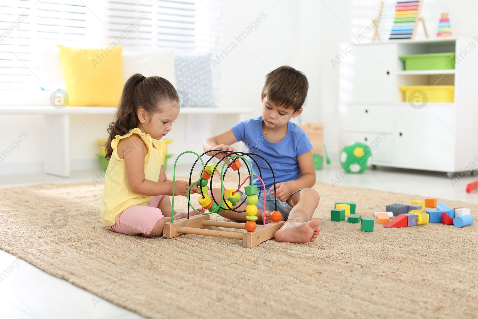 Photo of Cute little children playing with bead maze on floor at home. Educational toy