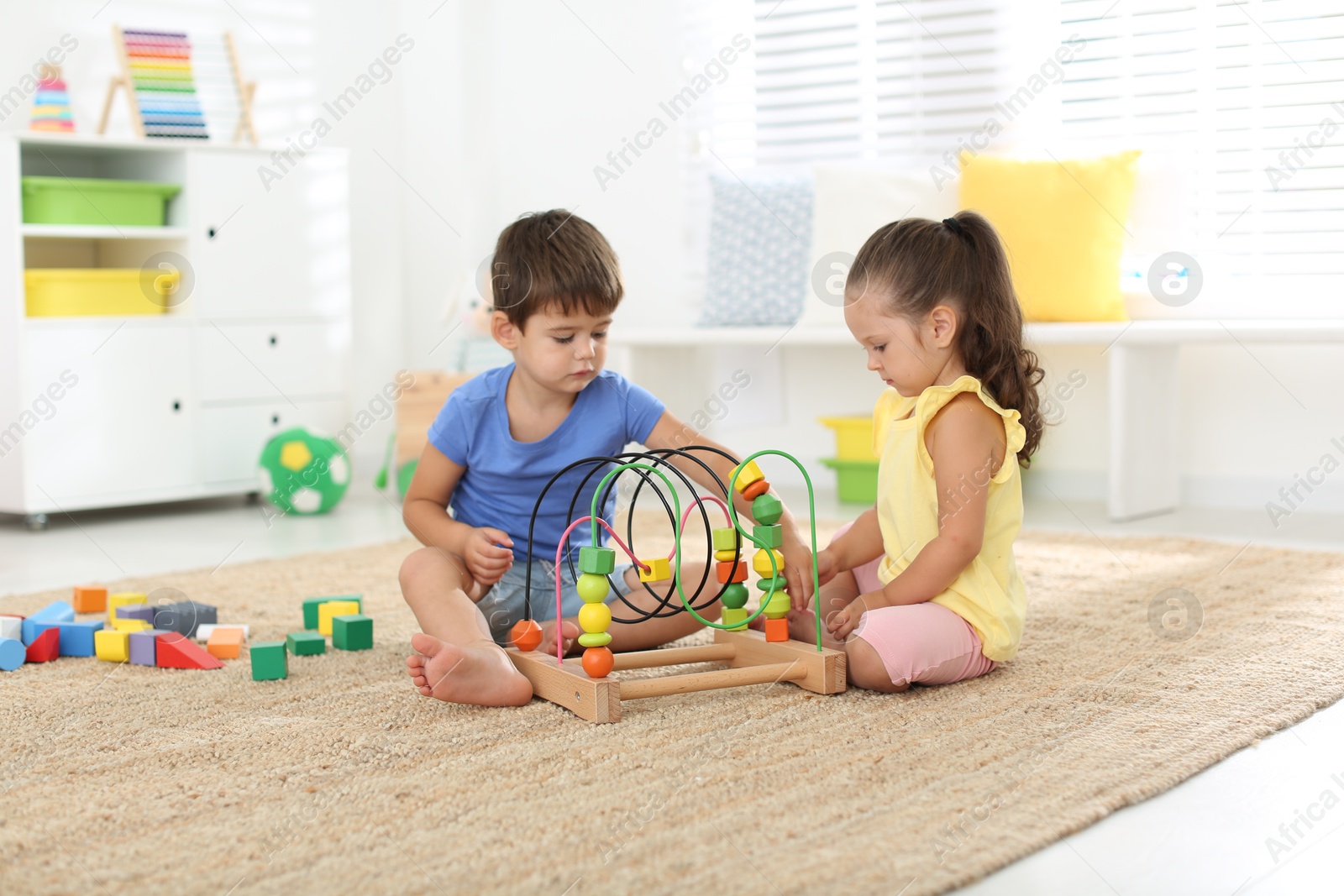 Photo of Cute little children playing with bead maze on floor at home. Educational toy