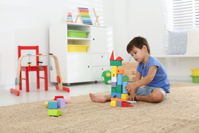 Photo of Cute little boy playing with colorful blocks on floor at home. Educational toy